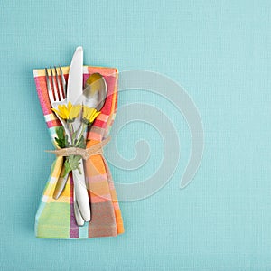 Summer or Spring Table Setting with teal tablecloth, silverware, and multicolor cloth napkin with yellow daisy flowers.  Backgroun photo