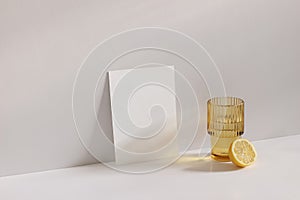 Summer stationery still life scene. Cut lemon fruit and golden rippled glass of water on beige table background in