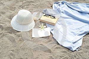 Summer still life. White straw hat on the sand of the mediterranean beach. Summer party invitation card mockup with white flower,