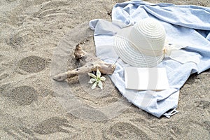 Summer still life. White straw hat on the sand of the mediterranean beach. Summer party invitation card mockup with white flower,