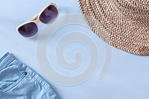 Summer straw hat beach, sunglasses  and shorts on light blue background. Copy space. Top view