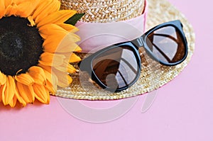 Summer straw hat, sunglasses and sunflower on pink background. close up.