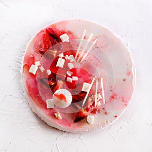 Summer strawberry mousse cake, fresh berries, coconut, and sweet decor element on top, white concrete background