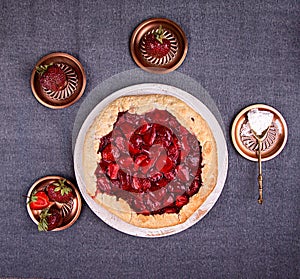 Summer strawberry pie cake galette and cooper saucer with strawberries over on gray background. Top view