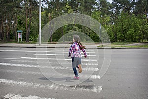 In the summer, on the street, a little girl crosses the road on a pedestrian crossing