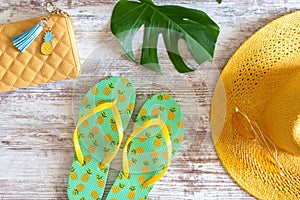 Summer style flat lay with pineapple flip flops and yellow sun hat