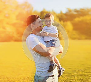 Summer sunny portrait of happy smiling young father holding little child son walking in the park together