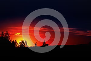 Summer sunset in a field in the sky of black bright colorful red orange color with clouds. The sun sets over the horizon against