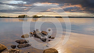 Summer sunset on the lake. Beautiful  water landscape with stones, sun reflection and cloudy sky