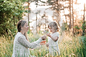 Summer sunset in the park or forest. Baby daughter on a piggy back ride with her mother.