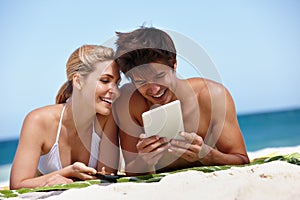 Summer surfing. Shot of a happy young couple watching something on their tablet at the beach.