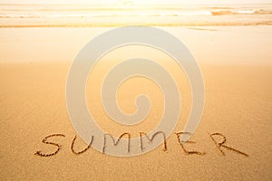 Summer - text written by hand in sand on a beach