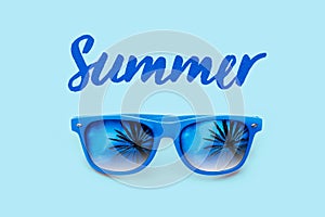 Summer textured blue text and blue sunglasses with palm trees reflections isolated in a light blue background