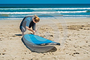 Summer time and active rest concept. Young surfer woman beginner fastens leash across leg, going to surf on big barral