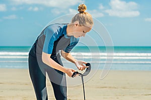 Summer time and active rest concept. Young surfer woman beginner fastens leash across leg, going to surf on big barral