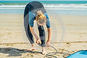 Summer time and active rest concept. Young surfer woman beginner fastens leash across leg, going to surf on big barral