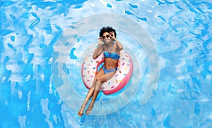 Summer time. Beautiful black woman in bikini swimming on inflatable ring at pool during tropical vacation, above view