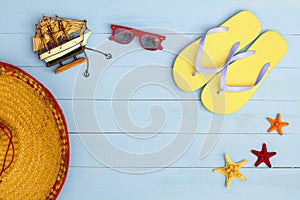 Summer time on a cool view on painted light blue wood table with sunglasses, flip flops, sailboat, hat and starfish