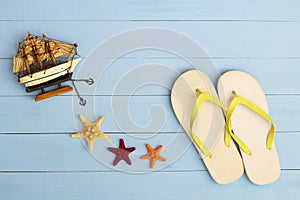 Summer time on a cool view on painted light blue wood table with sunglasses, flip flops, sailboat and starfish