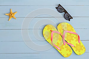 Summer time on a cool view on painted light blue wood table with sunglasses, flip flops and starfish