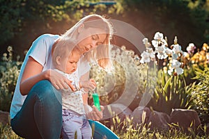 Summer time. Happy young mother hugs her baby daughter, who is playing with soap bubbles. Summer games with a child