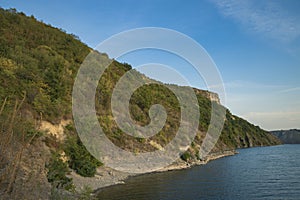 Summer time nature reservation landscape of green hill coast of lake water shoreline with blue sky background