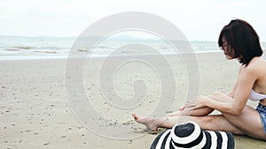 Summer time woman bikini use sunscreen lotion spf sunblock on the beach. Cheerful woman wear white bikini, short pant, straw hats