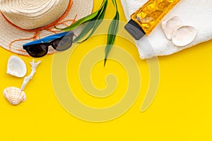 Summer travaling to the sea with straw hat, sun glasses, sunblock lotion on yellow background top view mock up