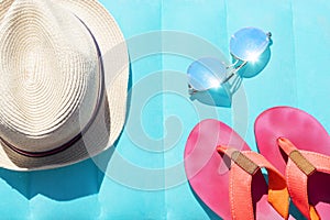 Summer travel accessories as sun hat, sun glasses, pink flip flops lie on bright swimming mattress.