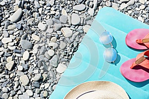 Summer travel accessories as sun hat, sun glasses, pink flip flops lie on bright swimming mattress on grey round sea stones.