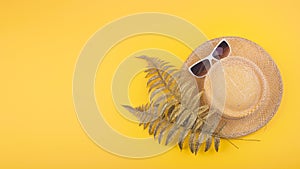 Summer travel vacation concept flat lay. Beach accessories, straw hat, golden tropical leaves and white sunglasses on yellow