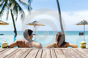 Summer travel vacation concept, traveler asian couple  with coconut relax in luxury infinity pool hotel resort with sea beach and