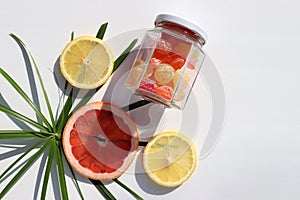 Summer tropical fruits and candies background. Flat lay composition with slices of red grapefruit, lemon, palm leaves, glass jsr