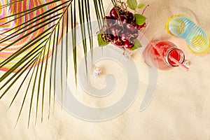 Summer tropical rest on sandy beach background - cold fruit drink, sun hat, slippers, slinky toy, cherries in box with palm leaf .