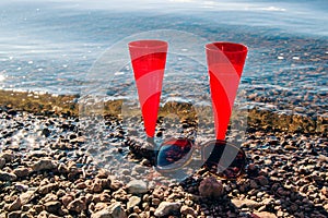 In summer, two red glasses of sparkling champagne or prosecco by the sea in sunglasses on a pebble beach