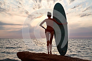 Summer vacation, beach time and adventure concept. Woman on rock with board for surfing waving with hand. Copy space