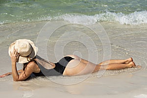 Summer vacation on beach. Woman in black swimwear lying on sandbeach. Girl enjoying sunbath near sea.