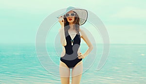 Summer vacation, beautiful young woman in bikini swimsuit and straw hat on the beach on sea coast background