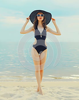 Summer vacation, beautiful young woman in bikini swimsuit and straw hat on the beach on sea coast background