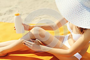 Summer vacation, close up of woman sunbathing and applying suntan cream on her legs lying on sand on the beach