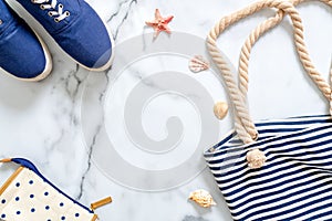 Summer vacation composition. Fashionable blue sneakers, striped beach bag, seashells, sea star on marble background. Women`s desk