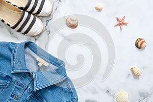 Summer vacation composition. Fashionable jeans jacket, striped summer sandals, seashells, sea star on marble background. Women`s d