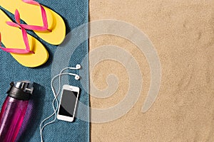 Summer vacation composition. Flip flops, smartphone and water bottle on sand background
