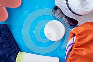 Summer vacation concept, accessories for summer travel flay lay on light blue background with a hat, sunscrin care cream and phone