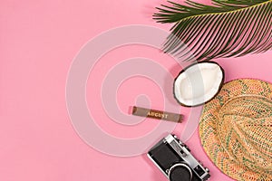 Summer vacation concept. Coconut, retro photo camera, hat and green palm leaves on pink background, flat lay