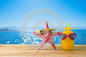 Summer vacation concept with cute starfish and pineapple juice with sunglasses over sea beach background