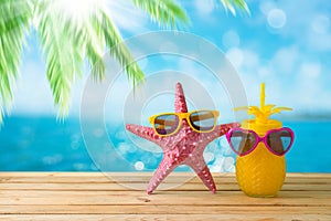 Summer vacation concept with cute starfish and pineapple juice with sunglasses over sea beach background