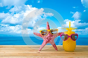 Summer vacation concept with cute starfish and pineapple juice with sunglasses over sea beach background