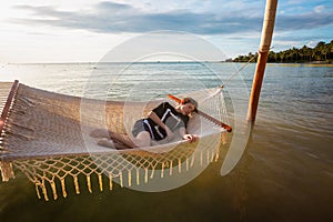 Summer vacation concept, happy caucasian teenage boy is relaxing in hammock in the sea at tropical beach in Vietnam