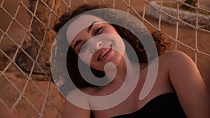 Summer vacation concept, happy woman in black swimsuit relaxing in hammock on tropical beach at sunset